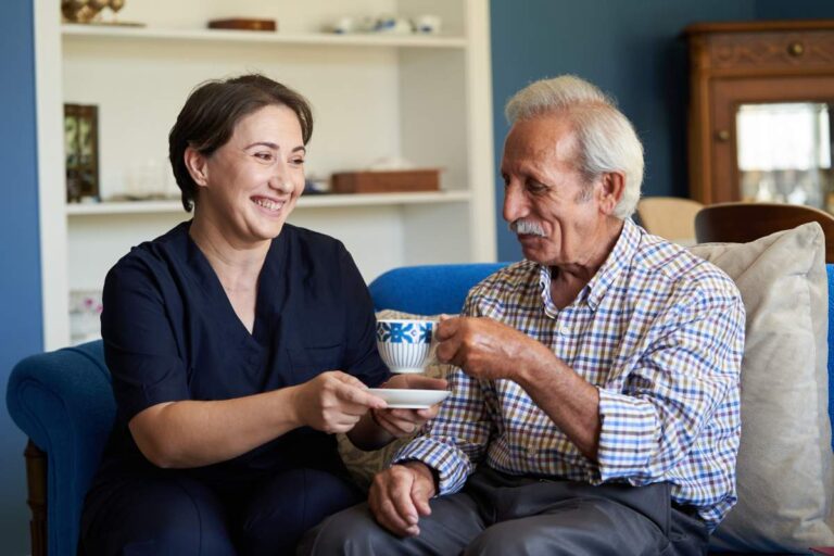 Two older adults following a gentle exercise routine together in a bright living room.